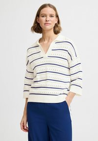 Hvid strikket sweater med marineblå vandrette striber, korte ærmer og V-hals. Har dekorative perforeringer overalt.