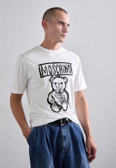 Valge puuvillane T-särk musta karu graafika ja "Moschino" tekstiga. Lahtine lõige, ümmargune kaelus, sobib siniste teksashortside ja vööga.