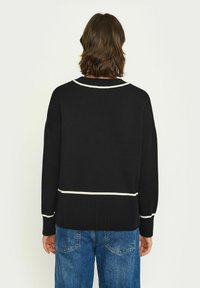 Pulover negru din tricot cu detalii de accent alb la guler și la tiv, având un croi lejer și mâneci lungi, asortat cu blugi.