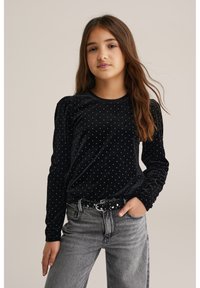 Fekete bársonyból készült, hosszú ujjú ing fehér pöttyökkel, puffadt ujjakkal. Szürke, magas derekú farmernadrággal és pöttyös övvel viselve.