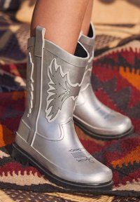 Silberne Gummistiefel mit schwarzen Akzenten, versehen mit einem Vogeldesign, strukturiertem Sohlenprofil und einer Lasche am oberen Teil zum einfachen Anziehen.