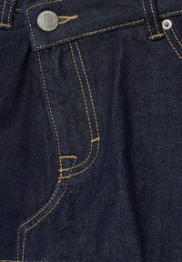 Tissu en denim bleu foncé avec des coutures contrastantes jaunes et un bouton en métal sur la ceinture près de la poche avant.