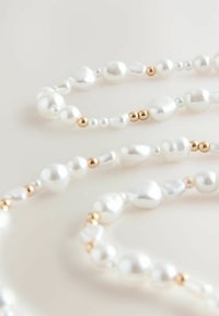 Colier din perlă, decorat cu perle albe neregulate și mărgele de aur, dispuse într-un model stratificat pe un fundal deschis.