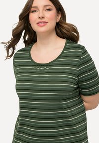 T-shirt verde a righe con scollatura a girocollo, caratterizzato da righe verticali e orizzontali in verde chiaro, grigio e nero. Morbido tessuto.