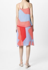 Plisséjurk met een gelaagd ontwerp in rood en lichtblauw. Verstelbare bandjes, vloeiende stof en een midilange silhouet.