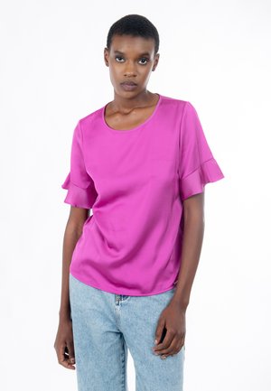 Top fucsia de manga corta con escote redondo y mangas con volantes; tela lisa y ajuste relajado. Combinado con vaqueros azules claros.