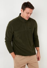 Pullover in felpa verde scuro con colletto a zip a un quarto, dotato di maniche lunghe e piccolo logo nero sul petto. Tessuto morbido e texturizzato.