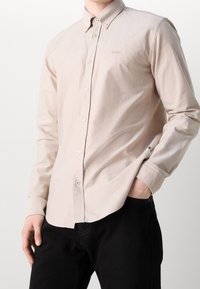 Lichtbeige button-up overhemd met lange mouwen, een spread collar en een gouden geborduurd logo. Heeft een klassieke pasvorm en een subtiele structuur.
