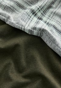 Grau kariertes Baumwollgewebe überlappt dunkles grünfarbene Baumwollgewebe und zeigt eine glatte Textur sowie eine gesäumte Kante mit kontrastierenden Mustern.
