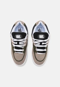 Vans sportbačiai su smėlio spalvos zomšiniu viršumi ir alyvuogių akcentais, juoda liežuvėlis, balti raišteliai ir guminis padas, su prekės ženklo etikete ant liežuvėlio.
