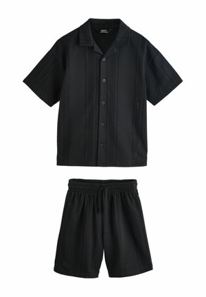 Čierna košeľa s krátkym rukávom na gombíky a zodpovedajúce elastické šortky so sťahovacou šnúrkou v páse, obe s jemnými perforovanými vertikálnymi pruhmi.