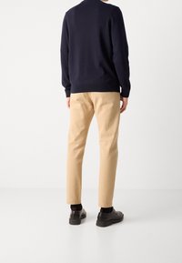 Morski sweter z okrągłym dekoltem, khaki tapered pants, czarne skórzane buty. Gładka faktura, dopasowany krój, widoczne kontrastowe stębnowanie na spodniach.