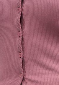 Rebrast top z vijugastim robom v mauve barvi in petimi roza gumbi na sprednji strani. Mehak material z oprijetim krojem.