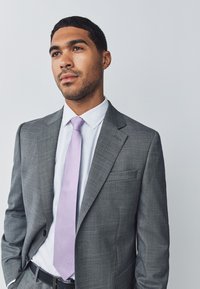 Gray suit in a textured fabric, white shirt, and a light purple tie. Slim-fit design with a single breast pocket and black belt.