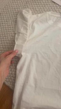 Valge puuvillane särk, mis on asetatud tekstuursele pinnale, rippuvate varrukatega ning sileda, kergelt kortsus kangasteksti ühik.