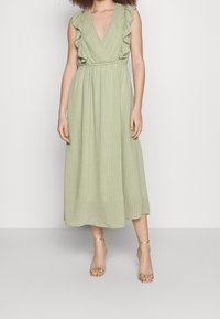 Vestido midi verde, acanalado, con mangas de hombros con volantes y diseño de escote en V. Incluye una cintura ajustada y una falda fluida.
