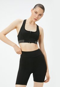 Sostenedor deportivo negro con cremallera frontal, tirantes anchos y acentos grises. Combinado con pantalones cortos de fitness negros de cintura alta, ajustados y con textura suave.