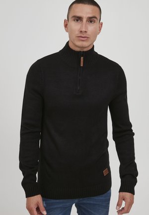 Schwarzer gestrickter Pullover mit hohem Kragen, der über einen halben Reißverschluss und gerippte Bündchen verfügt. Mit einer strukturierten Oberfläche und einem Leder-Logo-Patch am Saum.