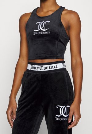 Kobieta ubrana w czarny aksamitny krótki top Juicy Couture i pasujące spodnie z białymi literami logo na klatce piersiowej i udzie.