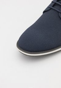 Mørkeblå joggesko med teksturert overdeler i stoff, rund tå, hvit gummi midtsåle og sort yttersåle. Har snøring og kontrasterende detaljer.