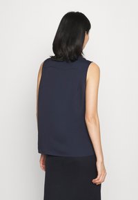 Námořnický bezrukávový top vyrobený z měkké látky, s vysokým výstřihem a uvolněným střihem. Obsahuje hladkou texturu a jednoduchý design.