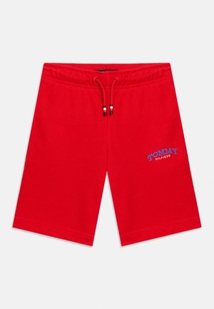 Shorts rouges mi-cuisse avec taille élastique, cordon de serrage et logo "Tommy Hilfiger" brodé en bleu et blanc sur la jambe gauche.