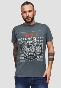 Harmaa puuvillainen t-paita, jossa on vintage-moottoripyöräkuva, ympäröitynä tekstillä "BSA MOOTTORIPYÖRÄKLUBI RIDERS SINCE 1903" erottuvilla väreillä.