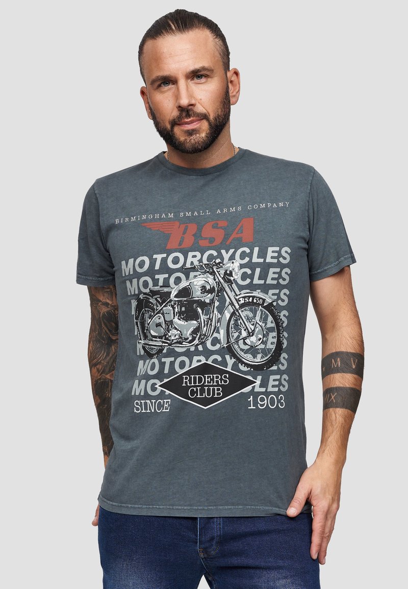 Harmaa puuvillainen t-paita, jossa on vintage-moottoripyöräkuva, ympäröitynä tekstillä "BSA MOOTTORIPYÖRÄKLUBI RIDERS SINCE 1903" erottuvilla väreillä.