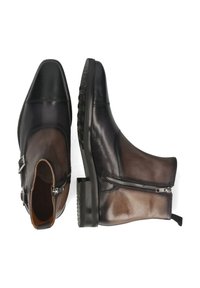 Botas de hombre de cuero bicolor hasta el tobillo con cremalleras y hebillas, una mostrada desde arriba y la otra en perfil lateral, sobre un fondo blanco.
