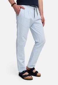 Pantalones de rayas azul claro y blancos con pliegues, cinturilla con cordón, bolsillos laterales y ajuste slim, combinados con sandalias negras.
