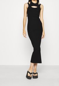 Mustapuku, sovitettu midi-mekko, jossa on korkea kaulus, leikkauksen yksityiskohta rinnassa ja spagettiolkaimet. Sileä rakenne, minimalistinen muotoilu.