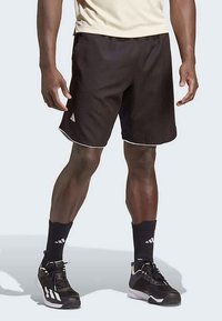 Sorte atletiske shorts med hvide detaljer, lavet af letvægtsstof, har en elastisk talje og sidelommer. Bæres med sorte sokker og sko.