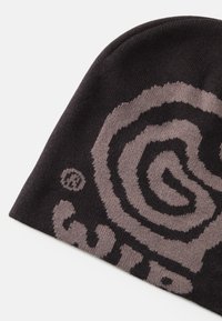 Beanie nero lavorato a maglia con design a spirale grigia e dettaglio del logo. Il tessuto è morbido e ha una texture liscia. Forma aderente, senza cuciture visibili.