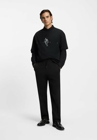 Schwarzes kurzärmeliges Hemd mit Grafikdruck, darüber ein schwarzes langärmeliges Hemd getragen. Kombiniert mit schwarz gestreiften Hosen und schwarzen Schuhen.