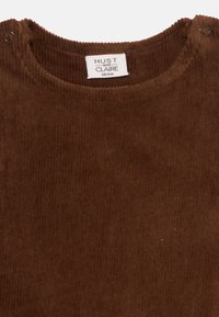Brown corduroy top with a round neckline, featuring snap buttons at the shoulder and a textured ribbed pattern. Label reads "HUST and CLAIRE."