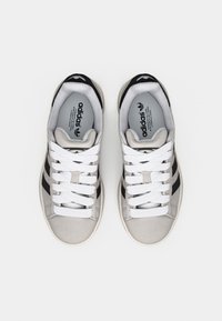 Szürke Adidas sportcipőpár fekete csíkokkal és fehér fűzőkkel, felülről nézve, fehér háttéren.