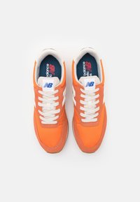 Baskets rétro orange mêlant nylon et suède, avec des accents blancs, une semelle intermédiaire beige et des lacets passant par des œillets en tissu.