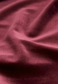 Tissu bordeaux avec une texture douce et lisse et un léger éclat, présentant de doux plis et une apparence légèrement moelleuse.