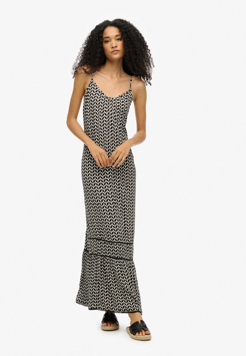 Schwarzes und weißes gemustertes Maxikleid mit Spaghetti-Trägern, ausgestattet mit einem ausgestellten Saum und leichtem Stoff. Getragen mit schwarzen flachen Sandalen.