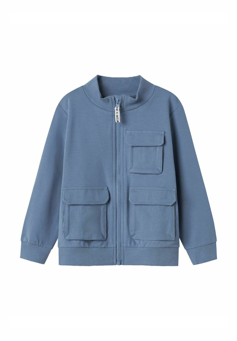 Chaqueta azul con cremallera, hecha de un tejido suave, que presenta un alto cuello, dos bolsillos frontales y puños acanalados en las mangas y el dobladillo.