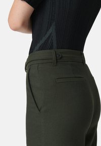 Pantaloni su misura verde oliva con una trama a spina di pesce, dotati di chiusura con bottone, tasche laterali e una cintura liscia.