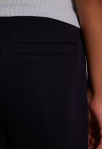 Helles marineblaues, lässig geschnittenes Paar Hosen mit einer strukturierten Baumwoll-Oberfläche, das eine einzelne Gesäßtasche und einen gerippten Bund aufweist.