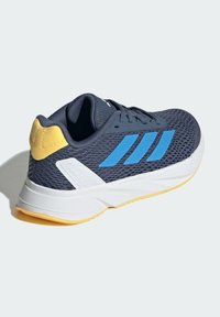 Zapatilla deportiva masculina con parte superior de malla azul marino, rayas azules, entresuela blanca y acento en el talón amarillo. Presenta un diseño texturizado para una mejor transpirabilidad.