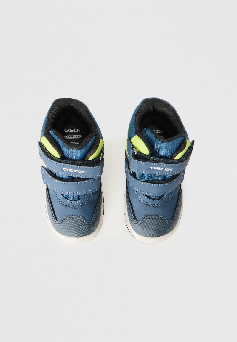 Chaussures pour enfants bleu et gris avec une surface texturée, deux straps Velcro réglables et des accents verts au niveau du talon. Design de semelle flexible.