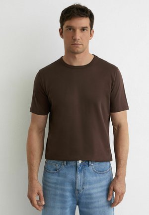 Brun bomulds-T-shirt med rund hals og korte ærmer, med en klassisk pasform. Båret med lyseblå jeans. Enkel design, glat tekstur.