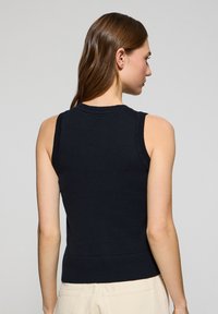 Marinblå  ärmlös stickad topp med ribbad krage och fåll, som visar en åtsittande design och slät textur. Bakvyn avslöjar detaljer på axlarna.