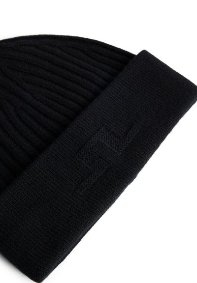 Bonnet en tricot noir avec une texture côtelée et un revers replié. Présente un logo en relief subtil sur le revers. Matière douce et chaude.