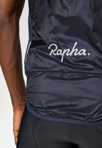Granatowa kamizelka rowerowa wykonana z lekkiego, błyszczącego materiału. Posiada ściągacz u dołu oraz biały logo "Rapha." z tyłu.