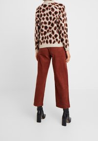 Leopardenmuster-Pullover mit geripptem Saum, kombiniert mit weiten, rostfarbenen Cordhosen und schwarzen Blockabsatz-Stiefeln.