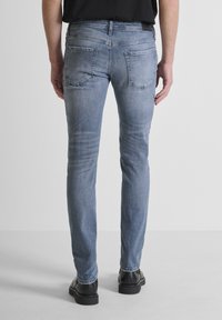 Tanke plave traperice uskog kroja s izblijedjelim završetkom, pet džepova i kontrastnim šavovima, nosi se s crnim cipelama, pokazujući ravni kroj nogavica.